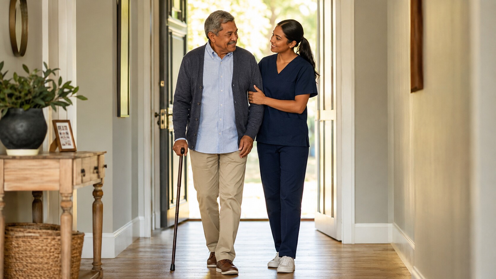 A caregiver supporting a senior with a cane on a short walk down a home hallway